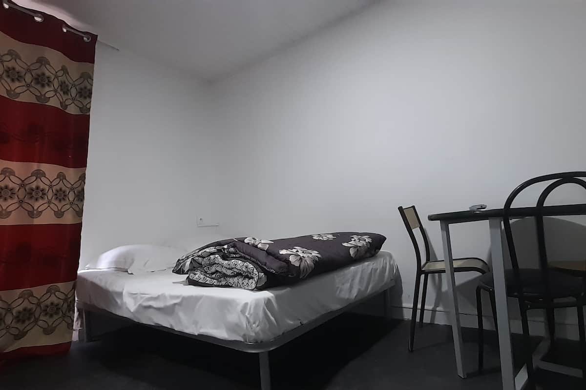 Una habitación pequeña y poco amueblada con una cama individual, una silla y una cortina.