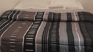 A bed with a striped blanket and pillows, a plain wall, and a wooden floor. - Hôtel des Andelys (Paris)