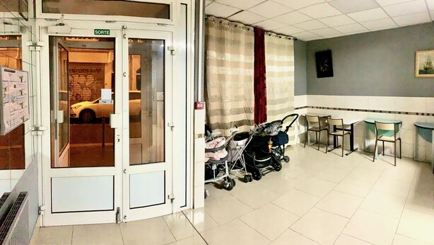 A lobby with a revolving door, a waiting area with chairs and a table, and a view of a parked car outside. - Hôtel des Andelys (Paris)