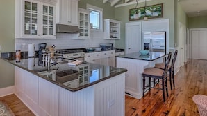 Una cocina con armarios blancos, encimera de granito y una isla grande con taburetes de bar.