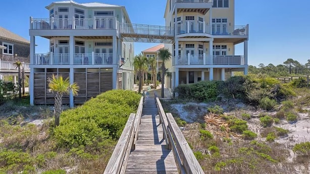 Una propiedad frente a la playa con un paseo marítimo de madera que conduce a un edificio de varios pisos con balcones.