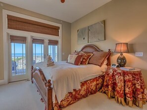 Un dormitorio con cama, mesita de noche con lámpara y vista al océano a través de amplias ventanas.