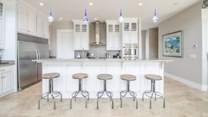 A modern kitchen with white cabinets, a central island with bar stools, stainless steel appliances, and pendant lighting.