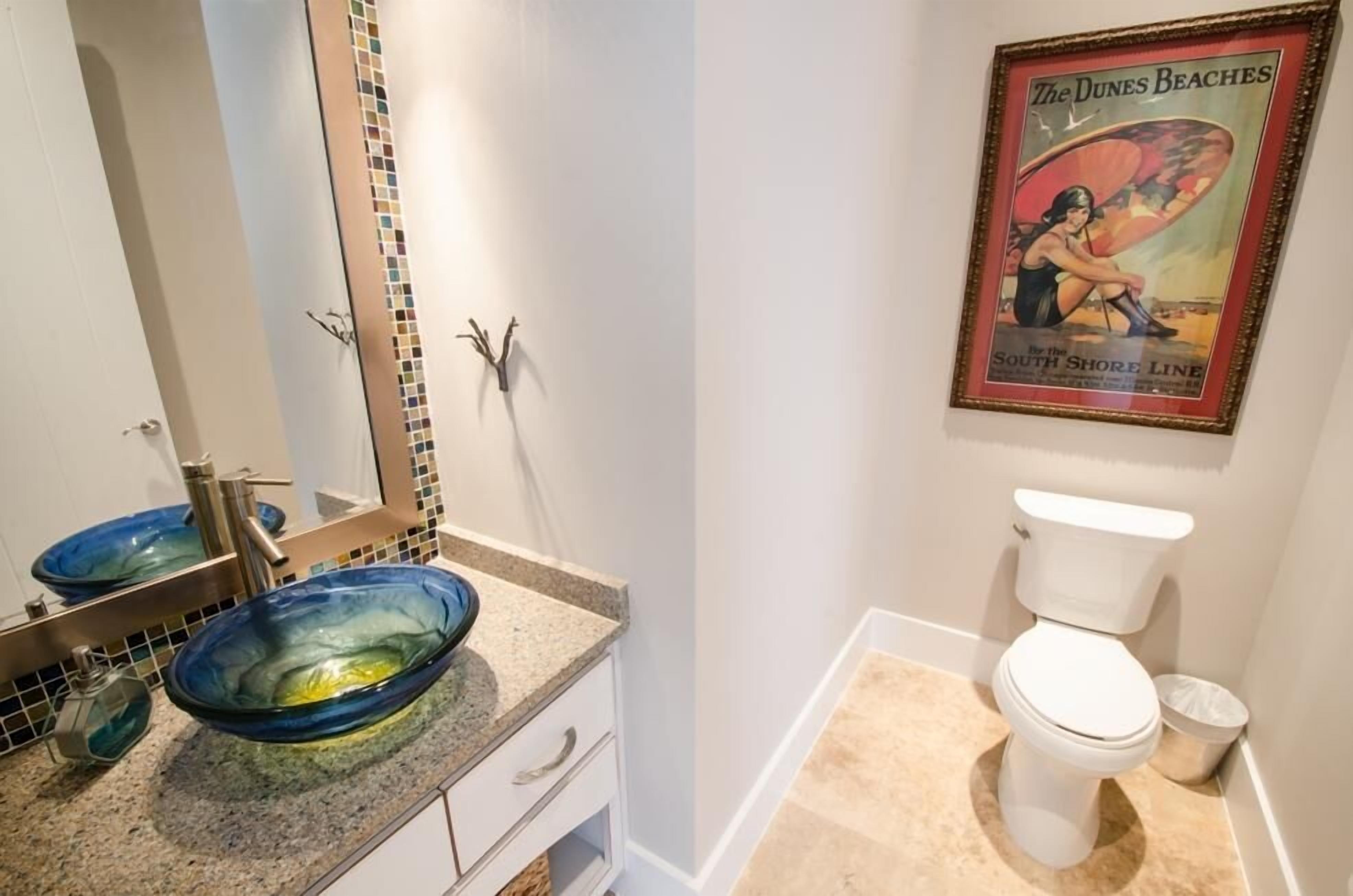 A bathroom with a white toilet, a blue glass sink, and a framed poster on the wall.