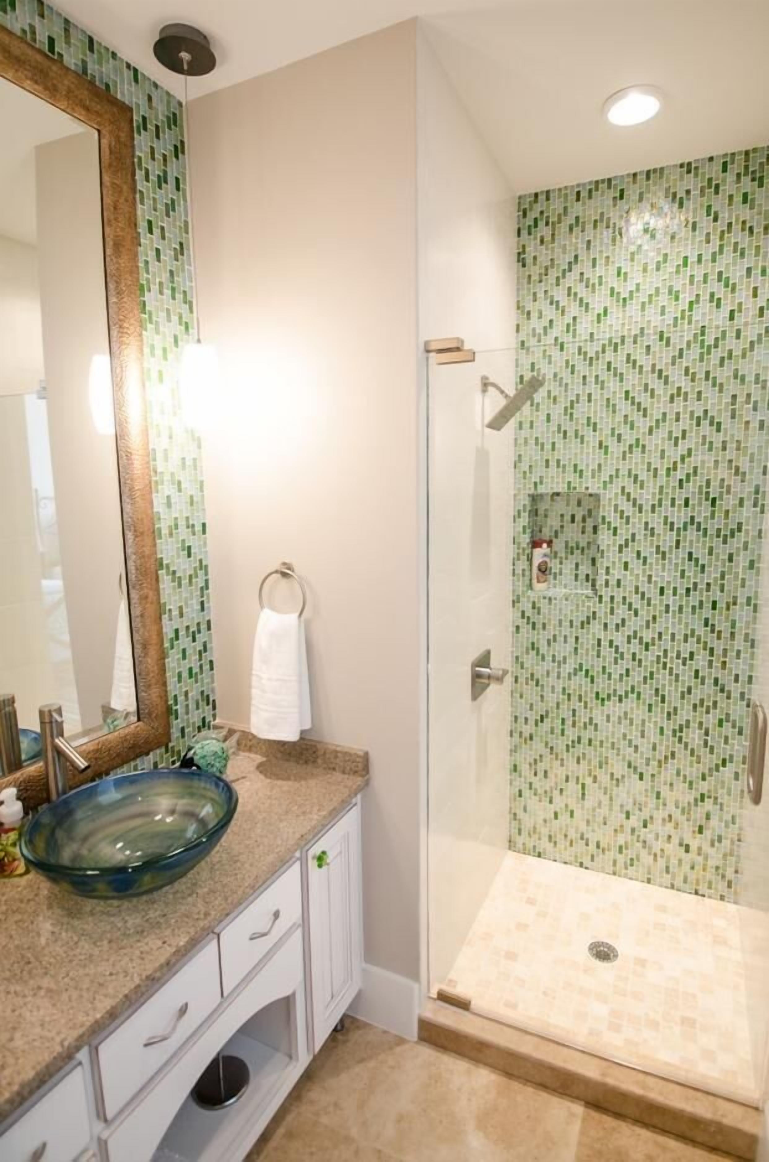 A bathroom with a glass shower enclosure, a large mirror, and a bowl sink.