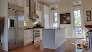 Una cocina moderna con armarios blancos, un refrigerador de acero inoxidable, una isla con pileta y un ventanal que proporciona luz natural.