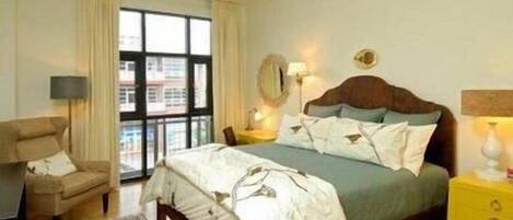 A bedroom with a large bed, a chair, a nightstand, a lamp, and a ceiling fan.