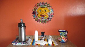 A kitchen counter with a coffee maker, a pitcher, a vase, and a decorative wall piece. - El Patio Inn (San Angelo)