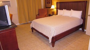 A hotel room with a bed, a desk with a computer, a chair, a lamp, and a window with curtains. - El Patio Inn (San Angelo)