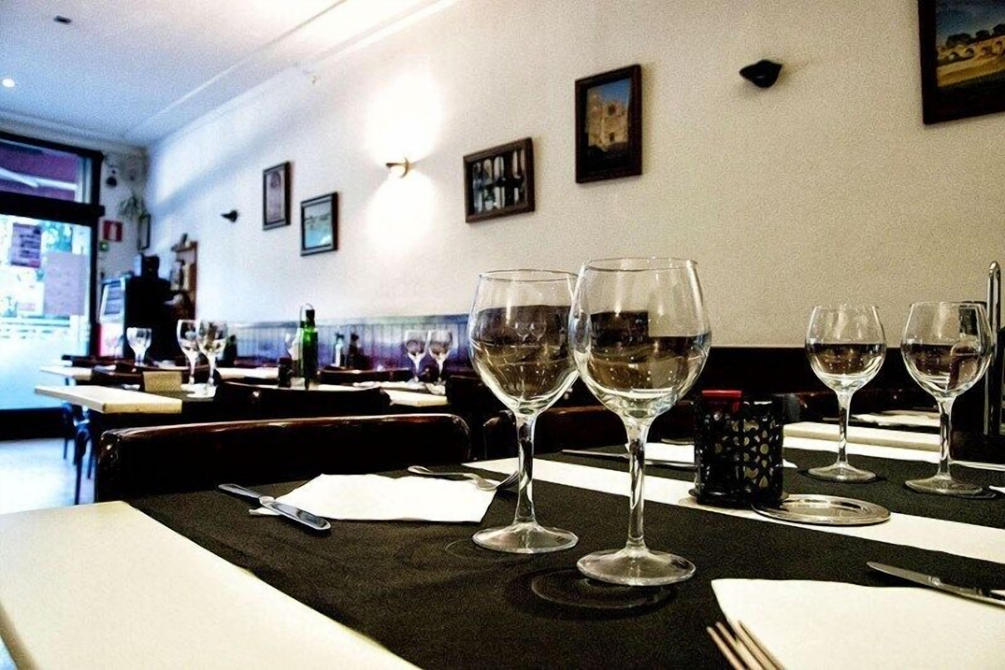 A restaurant interior with tables set for dining, featuring wine glasses and cutlery.