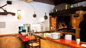 A kitchen with a brick oven, wooden bar stools, and a counter with plates and a basket. - Hostal Emporda (Castello d'Empuries)