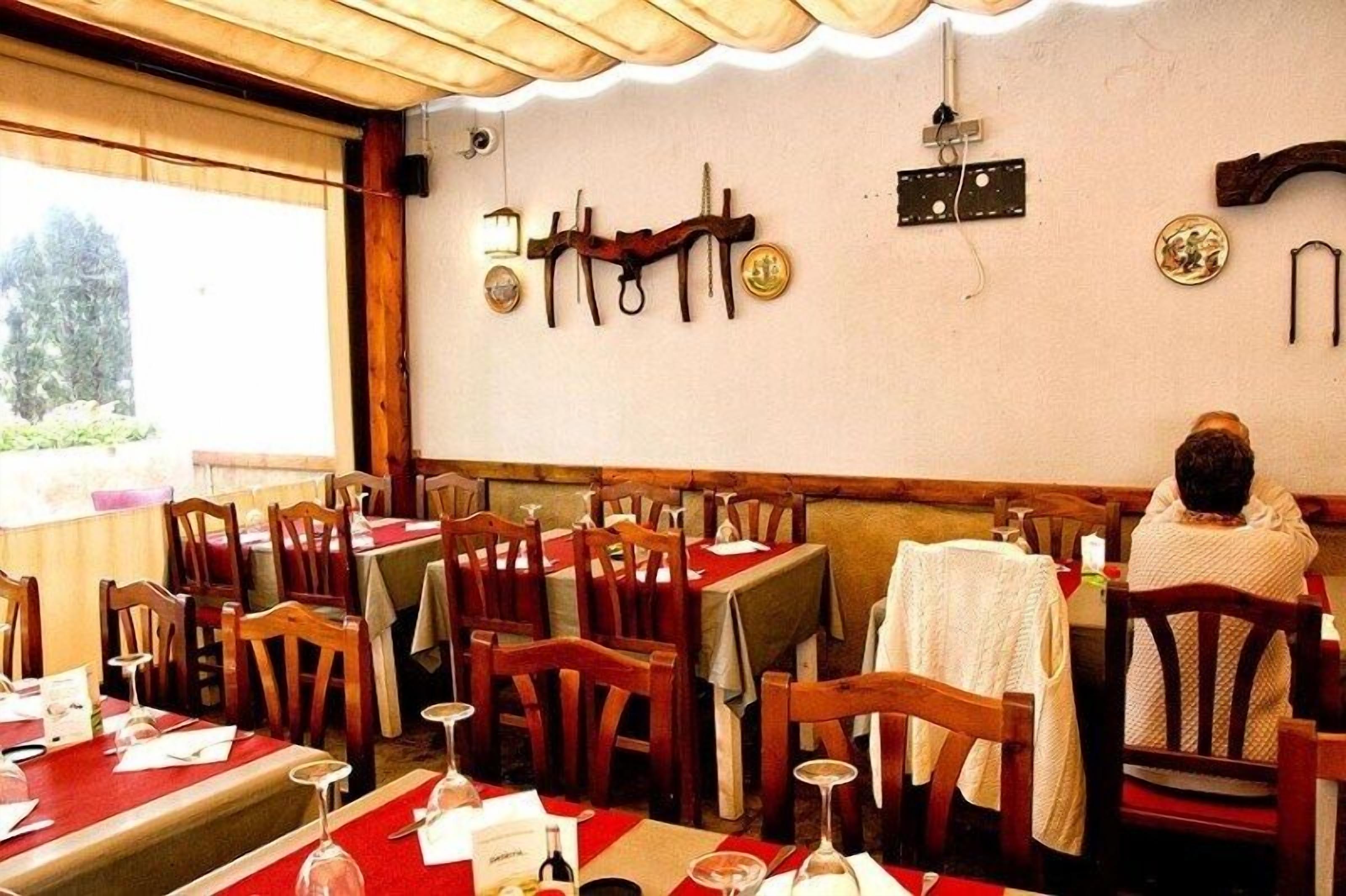 Een restaurant met houten tafels en stoelen, een persoon zittend aan een tafel, en aan het muur bevestigde objecten zoals een klok en een plaquette.
