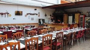 An outdoor dining area with multiple tables and chairs, a bar area, and a television mounted on the wall. - Hostal Emporda (Castello d'Empuries)