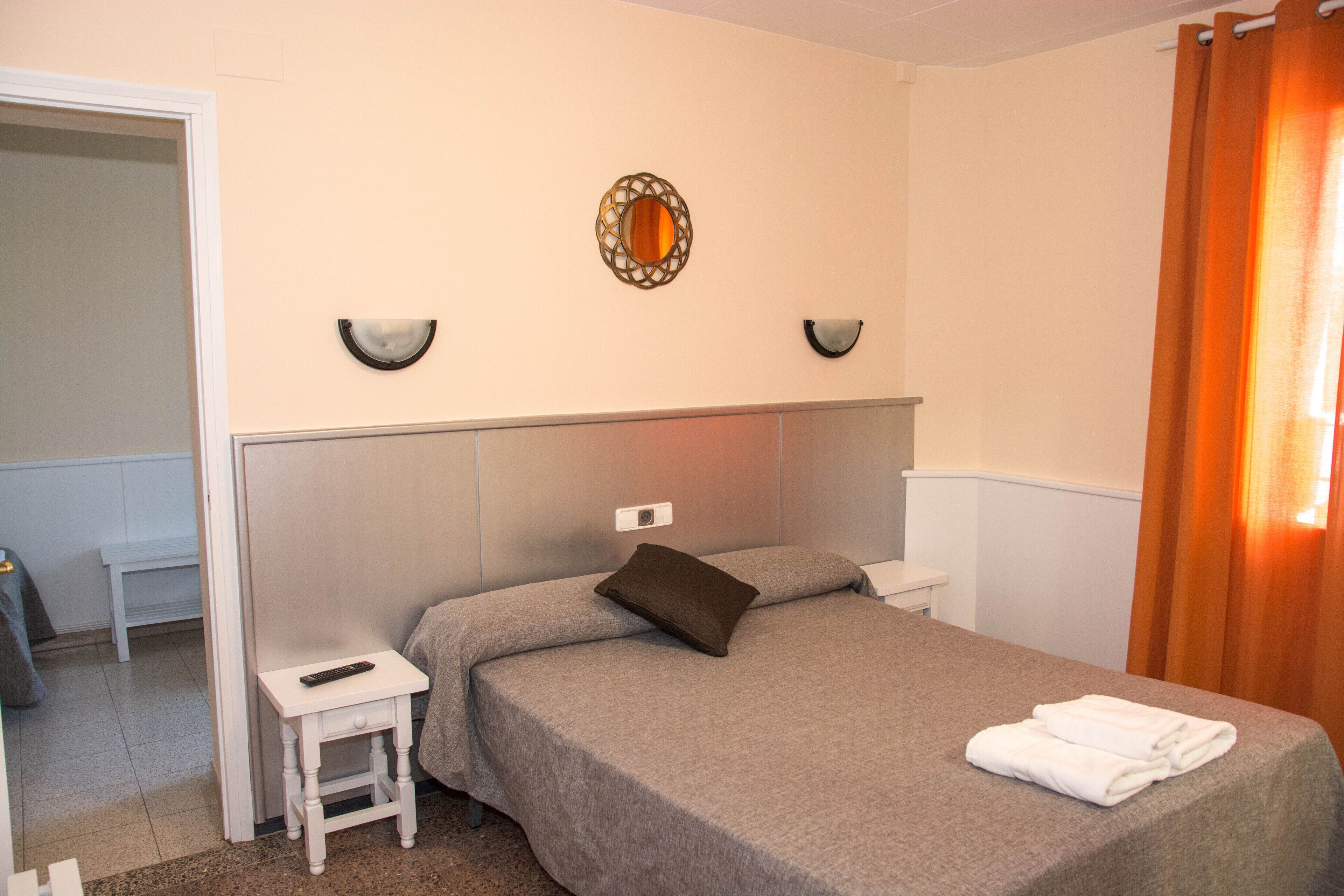 Una habitación de hotel con una cama, una mesita de noche, un espejo y una cortina.