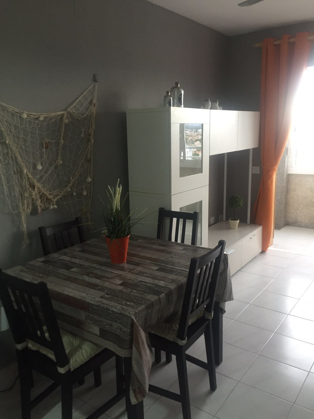 A dining area with a table set for six, surrounded by chairs. A potted plant is on the table, and there is a cabinet with a mirror above it.