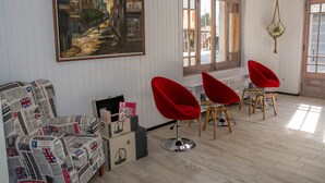 A room with a large painting, a red chair, a wooden table, and a window with a view of the street. - Hostal Emporda (Castello d'Empuries)