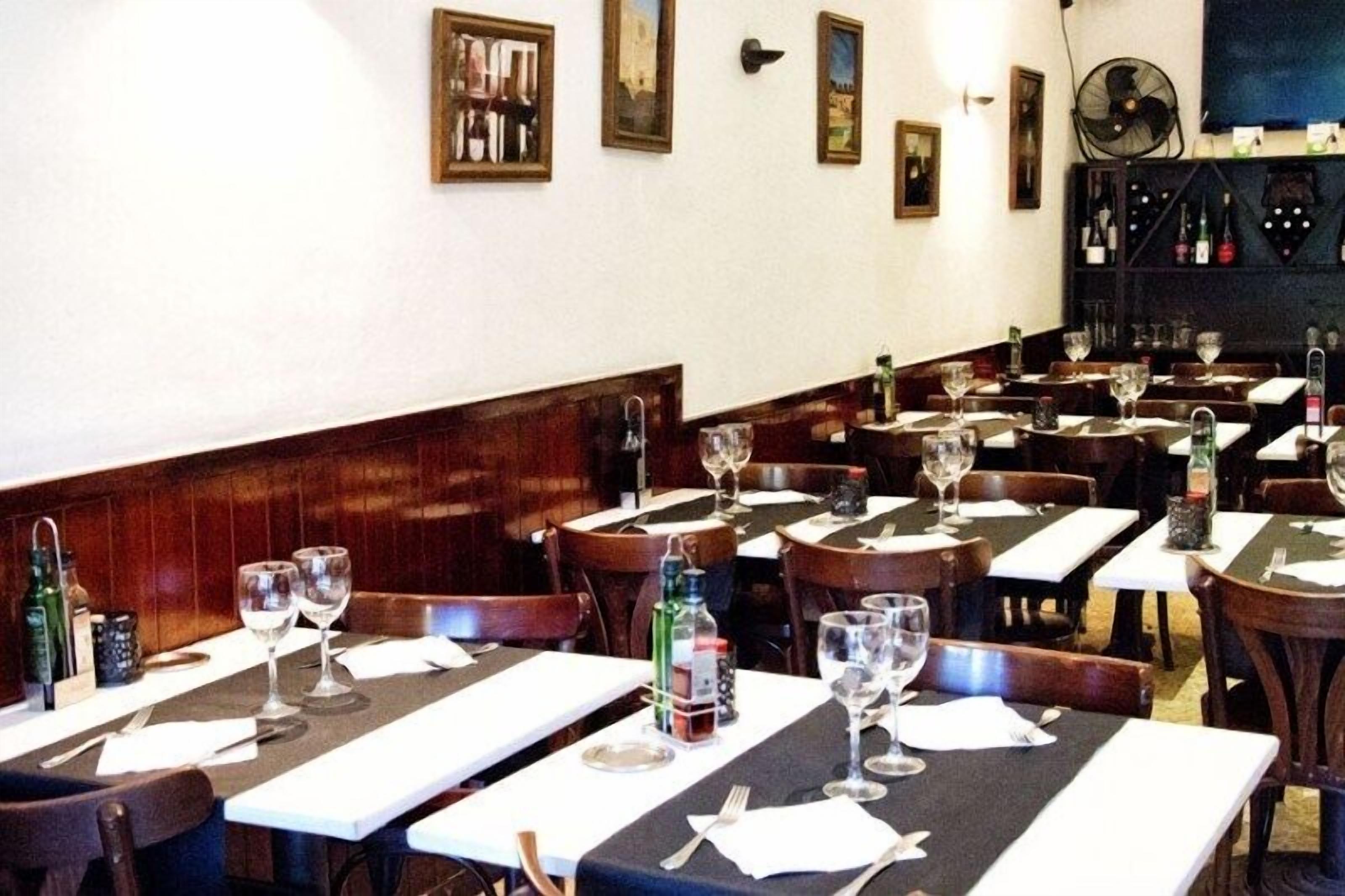 Um restaurante com várias mesas preparadas para refeições, cada uma com taças de vinho e talheres.