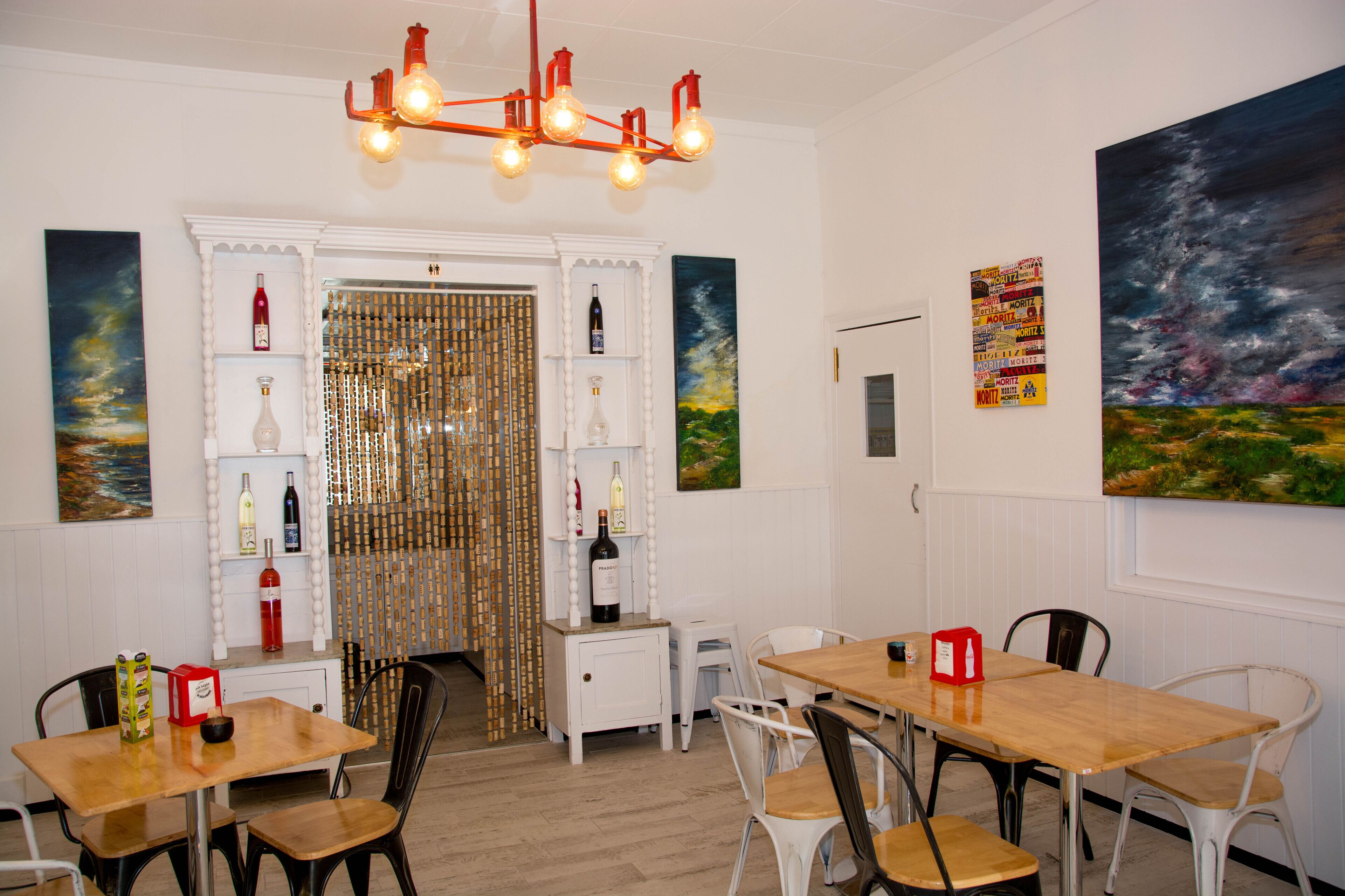 Un comedor con mesas y sillas de madera, una lámpara decorativa y obras de arte en las paredes.