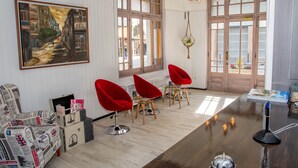 A modern interior with a wooden floor, red chairs, a painting, and a large window. - Hostal Emporda (Castello d'Empuries)