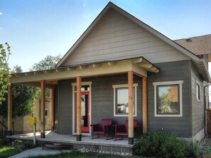 Une maison moderne à deux étages, dotée d’un porche abrité, d’une porte rouge et d’un petit espace extérieur aménagé pour s’asseoir.