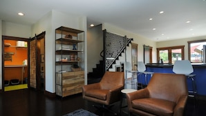 A modern living room with leather armchairs, a wooden bookshelf, and a staircase with a geometric railing. - Salida Modern 3 Bedroom Holiday Home By Pinon Vacation Rentals (Salida)