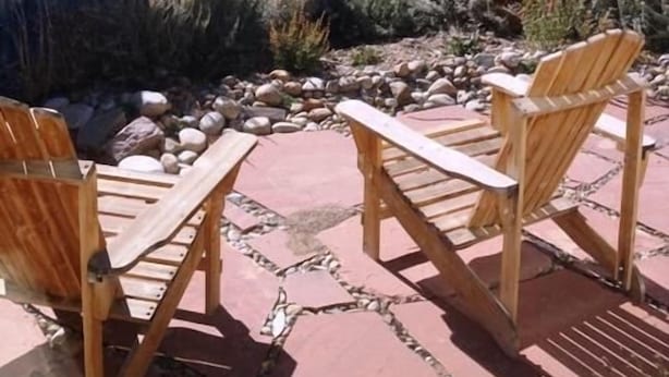 Eine Terrasse mit Holzbänken und einem Steinweg, umgeben von einem Metallzaun und einer Bergkulisse.