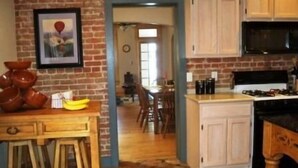 A kitchen with a brick wall, wooden cabinets, and a dining area in the background. - Scott s Downtown 1 Bedroom Holiday Home By Pinon Vacation Rentals (Salida)