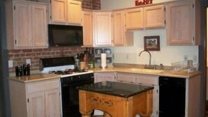 A kitchen with wooden cabinets, a microwave, a stove, a sink, and a wooden island. - Scott s Downtown 1 Bedroom Holiday Home By Pinon Vacation Rentals (Salida)