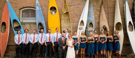A group of people standing in front of a brick building with several kayaks leaning against the wall.