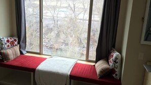A room with a large window, a red bench with pillows, and a white throw blanket.