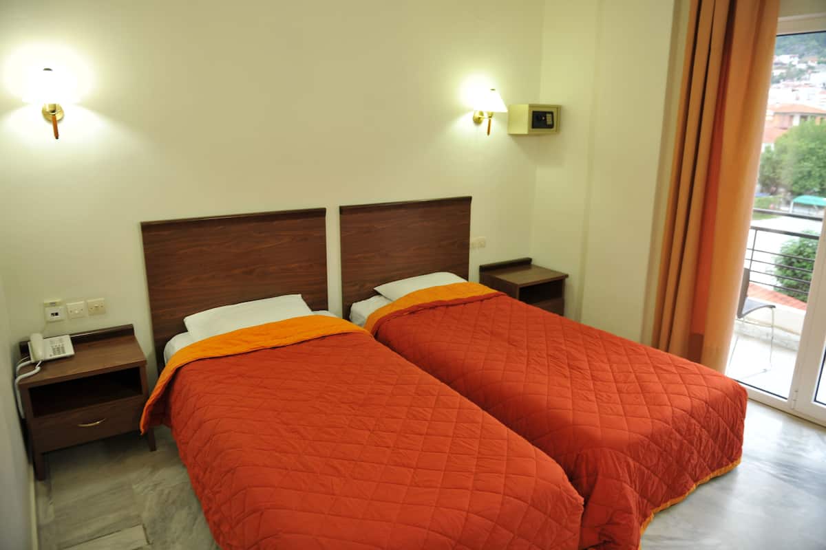 A hotel room with two beds, a nightstand with a phone, and a wall-mounted lamp.