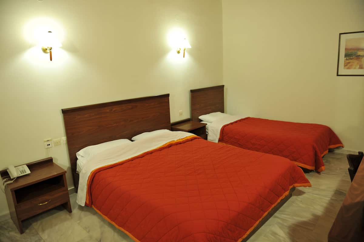 A hotel room with two beds, each with a wooden headboard, white bedding, and red blankets. There are bedside tables with lamps and a phone.