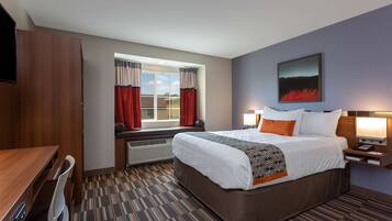 A hotel room with a bed, bedside table, lamp, window with curtains, and a painting on the wall.