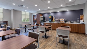 Una cafetería moderna con mesas y sillas de madera, una zona de cocina con electrodomésticos y una barra que exhibe productos alimenticios.