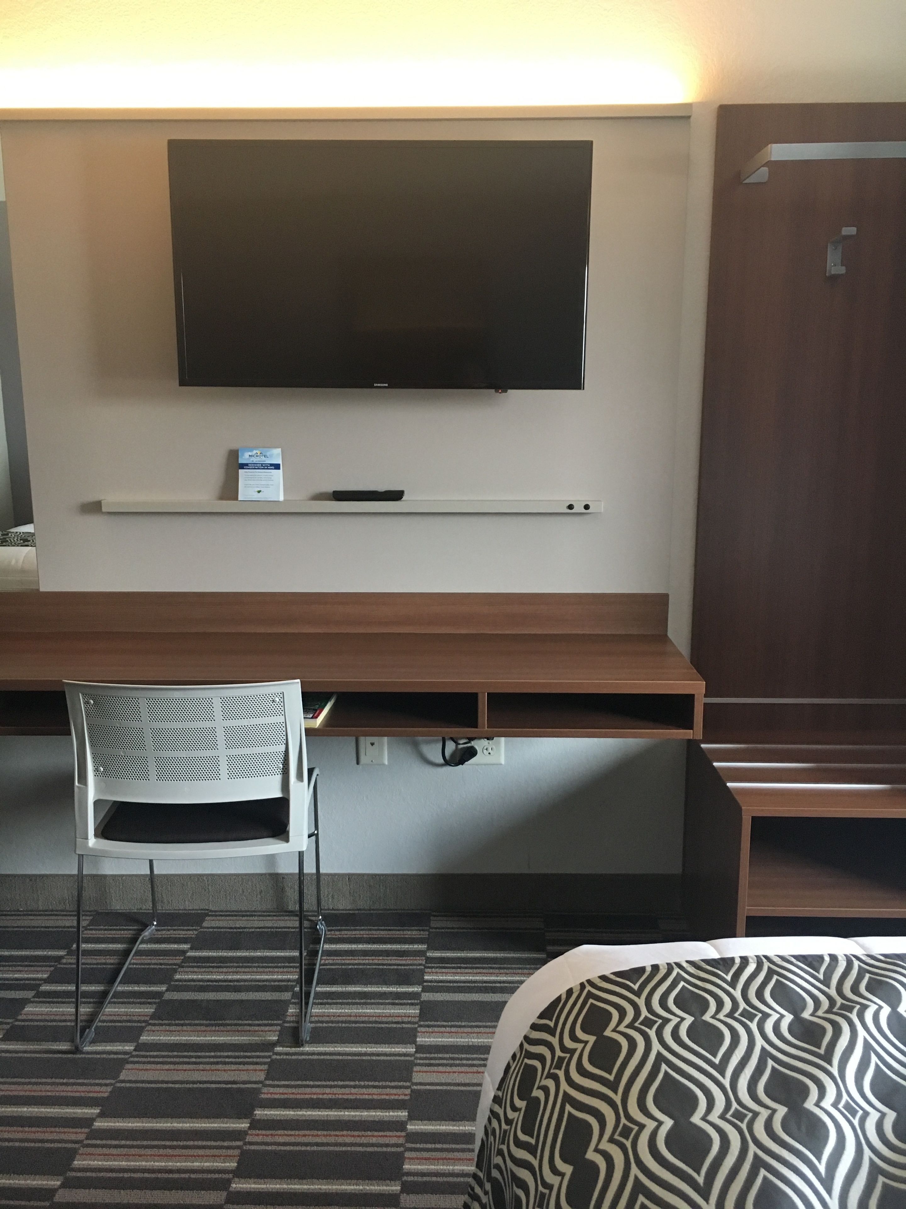 Camera d'albergo con TV a schermo piatto montata a parete, una scrivania con sedia e un letto con lenzuola decorate.