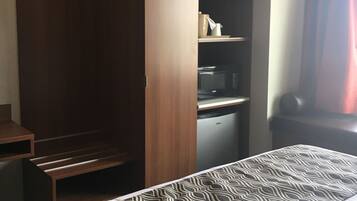 A hotel room with a bed, a wardrobe, a desk, and a microwave.