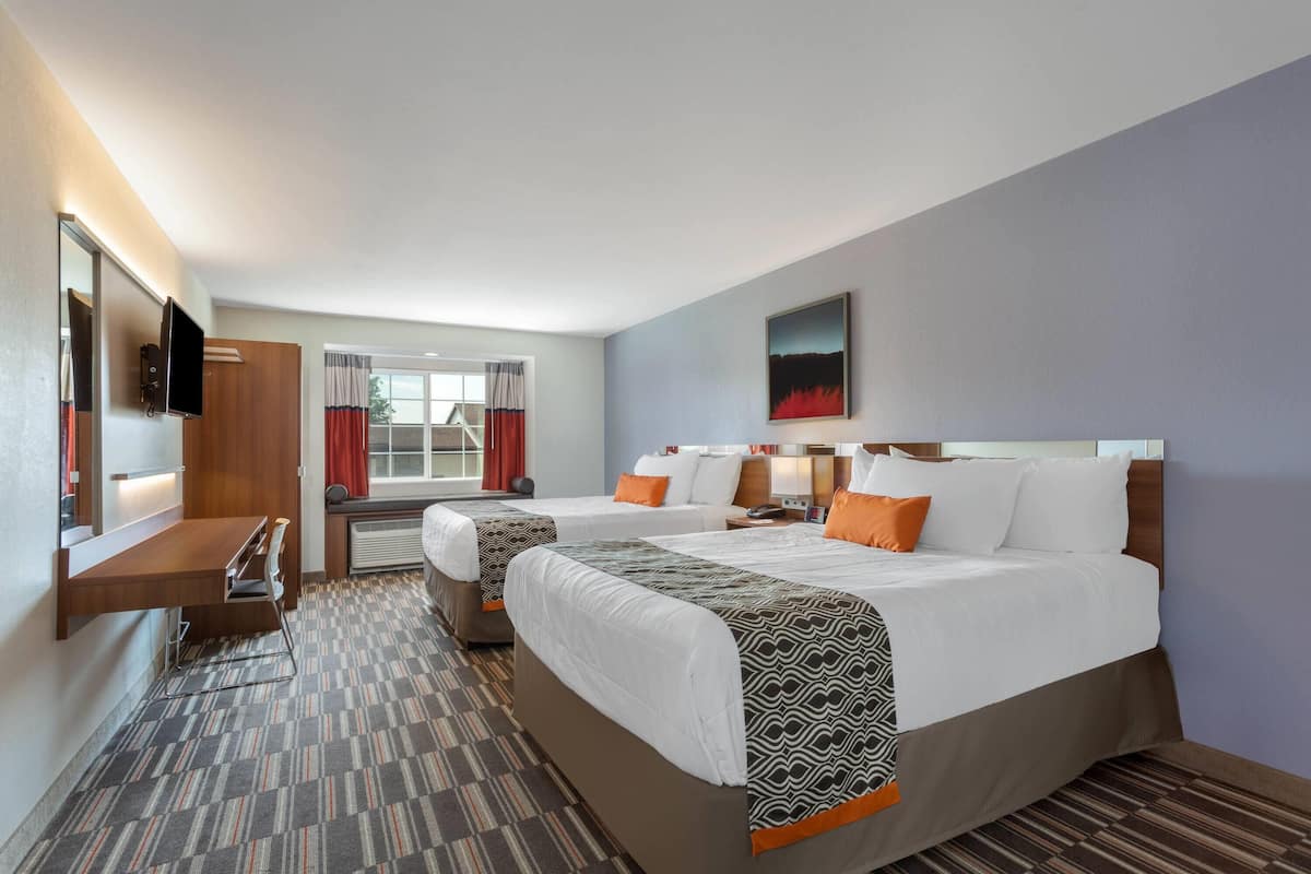 A hotel room with two beds, a desk, a TV, and a window with curtains.