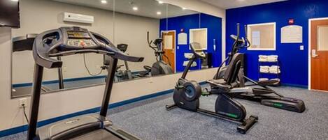 A gym with cardio machines, a mirror, and a blue wall with a door.