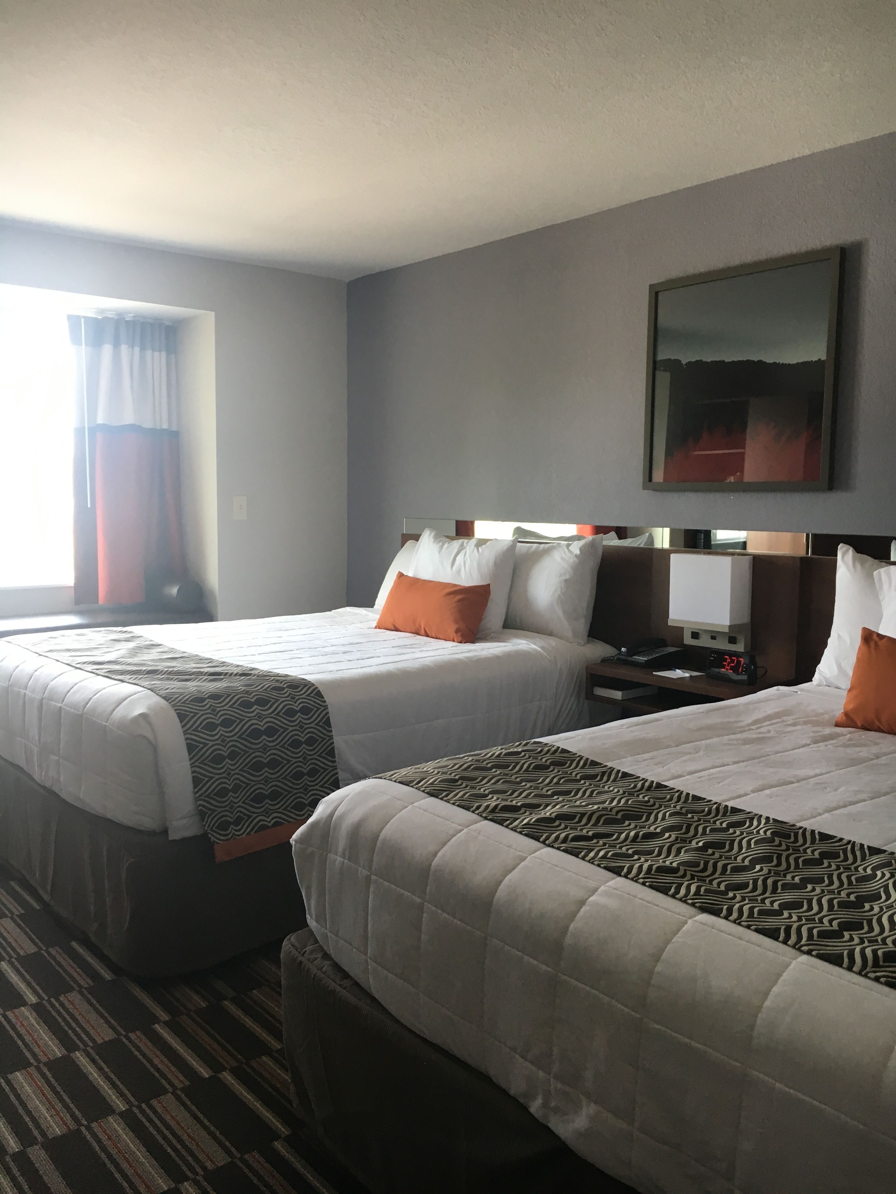 Habitación de hotel con dos camas, un escritorio, una silla, un reloj y una ventana con cortinas.