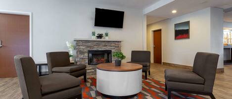 A modern lounge area with a stone fireplace, a flat-screen TV, and two armchairs.