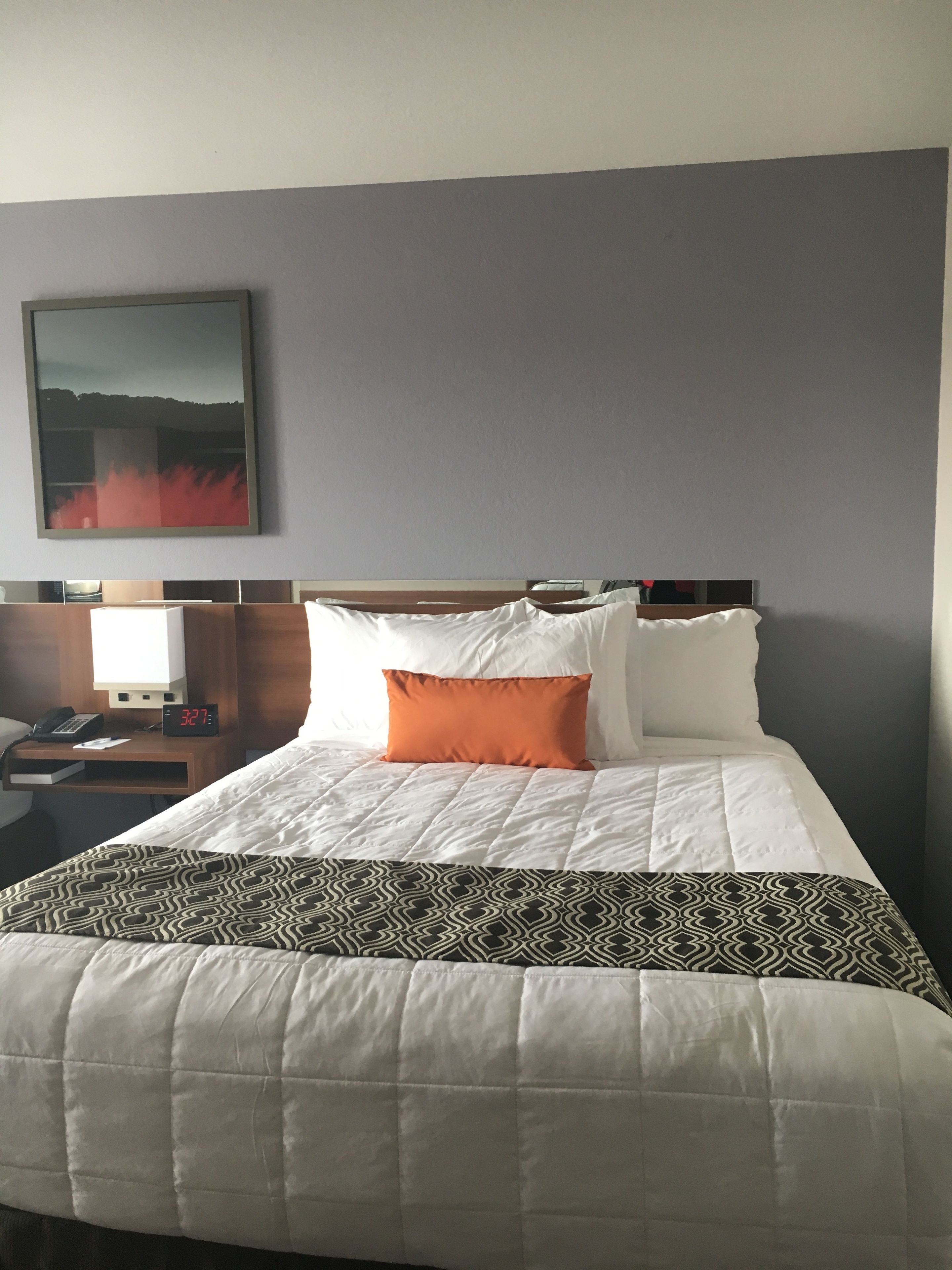 Ein Hotelzimmer mit Bett, Nachttisch, Lampe und einem Gemälde an der Wand.