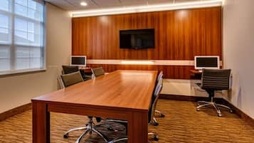 A conference room with a long wooden table, two chairs, a TV mounted on the wall, and two monitors on the table.
