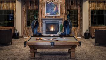 A pool table in a room with wooden paneling, a fireplace, and a chandelier.