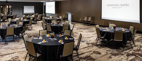 A conference room with multiple tables and chairs, a podium, and a large screen displaying "SPRINGHILL SUITES MARRIOTT".