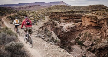 Un sendero de bicicleta de montaña accidentado con terreno rocoso y vegetación escasa.