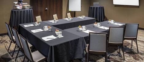 A conference room with two tables, chairs, a whiteboard, and a screen displaying "SPRINGHILL SUITES MARRIOTT".