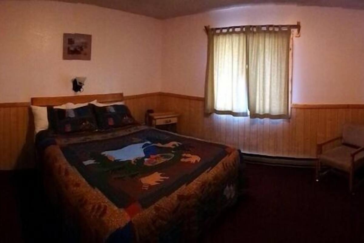 Un dormitorio con una cama, una silla, un ventanal con cortinas y un armario de madera.