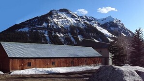 Un granero de madera con techo metálico, rodeado de nieve y un paisaje montañoso.