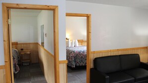 Una habitación con una cama, un banco de madera, un sofá negro y una puerta de madera.