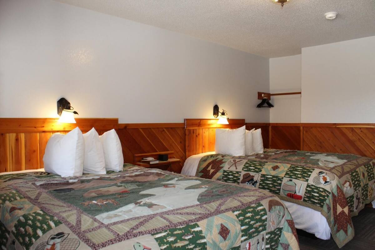 Una habitación de hotel con dos camas, cada una con cabecero de madera y colcha acolchada. Hay dos lámparas fijadas a la pared a cada lado de las camas.